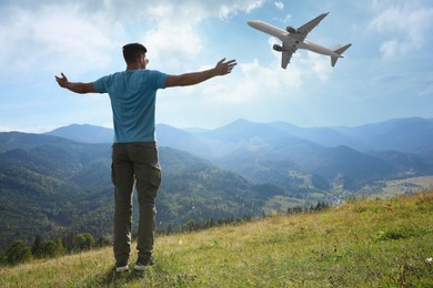 Man looking at airplane flying in sky over mountains, back view