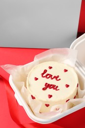 Photo of Tasty bento cake with Love You inscription in takeaway packaging on red table, closeup