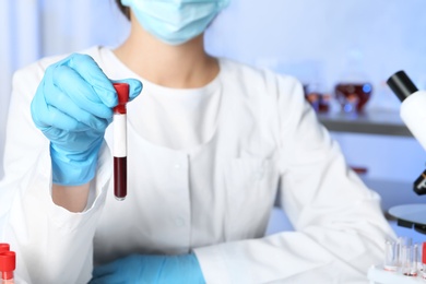 Laboratory worker holding test tube with blood sample for analysis, closeup