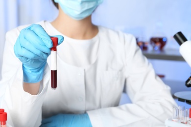 Photo of Laboratory worker holding test tube with blood sample for analysis, closeup