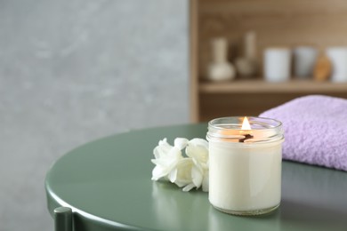 Photo of Scented candle, flowers and towel on green table indoors, space for text