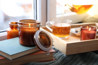 Photo of Burning candle on stack of books near window indoors