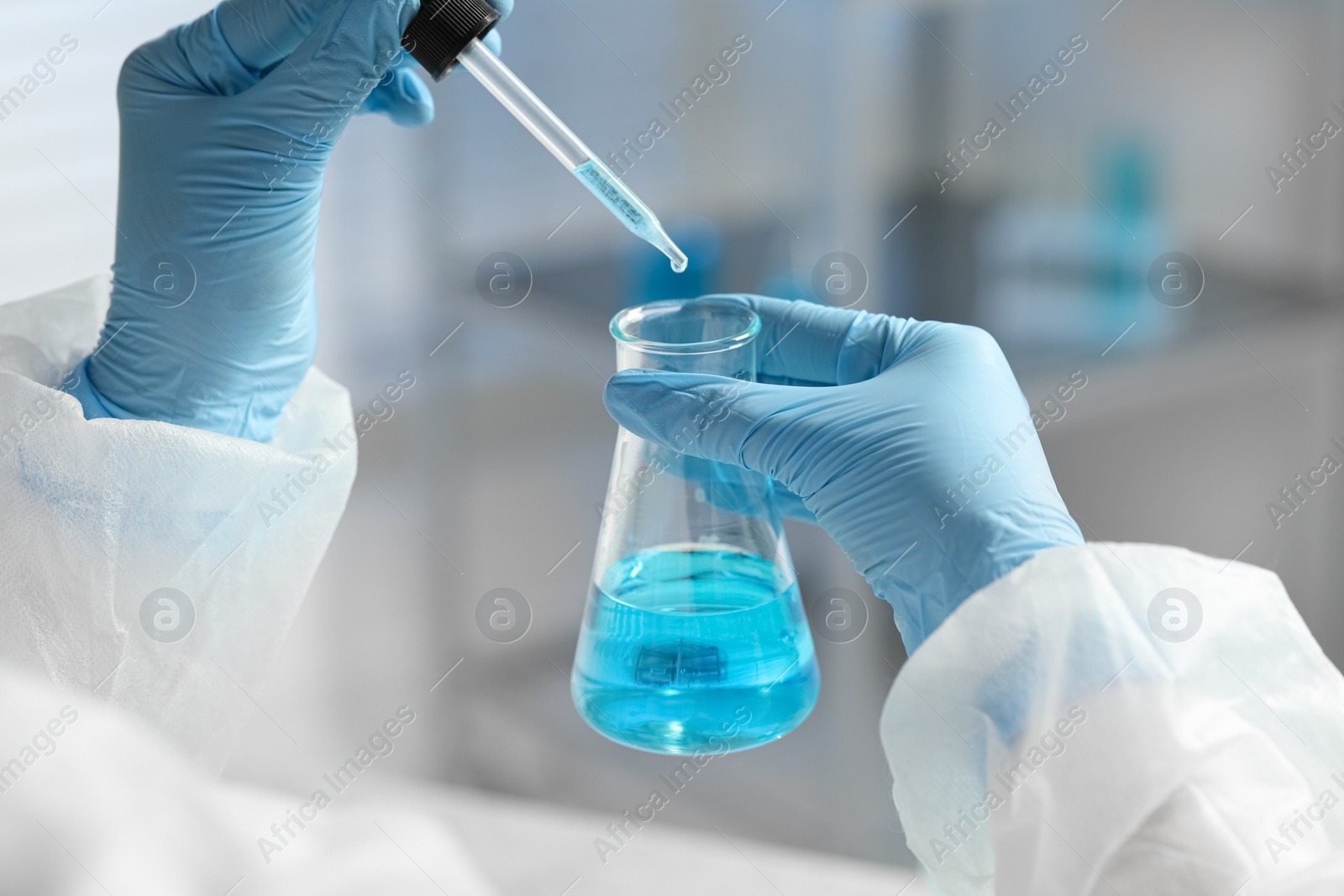 Photo of Scientist dripping liquid from pipette into beaker in laboratory, closeup