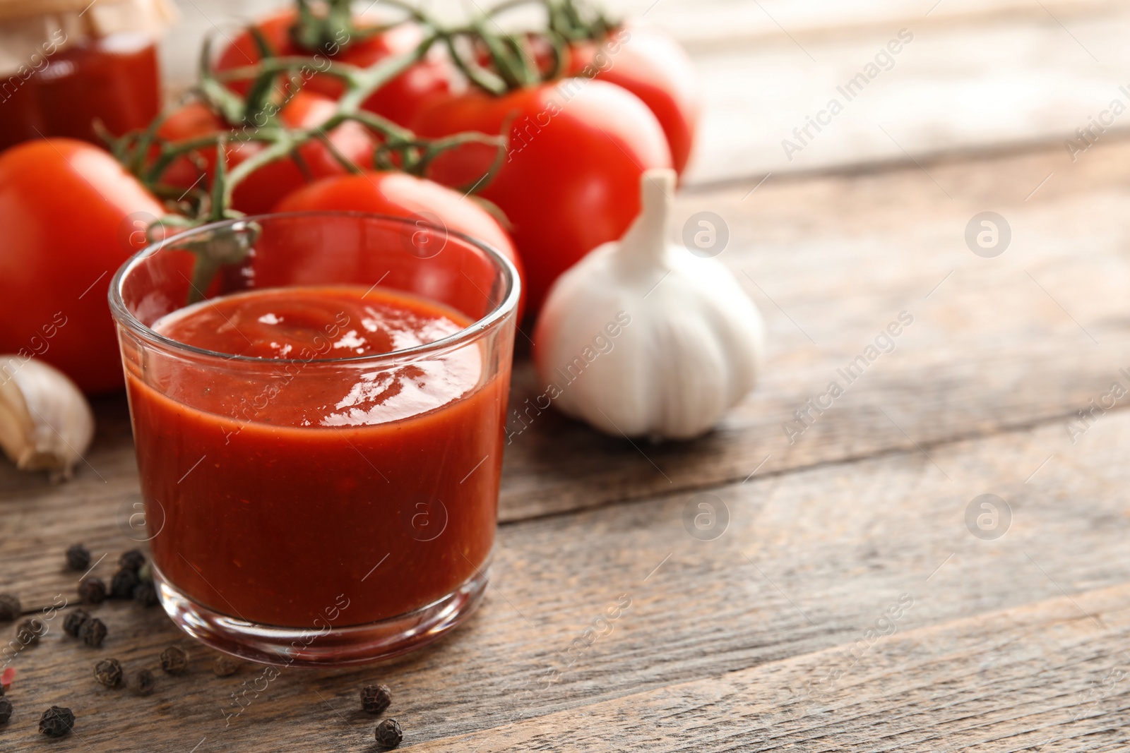 Photo of Composition with glass of tasty tomato sauce on wooden table. Space for text