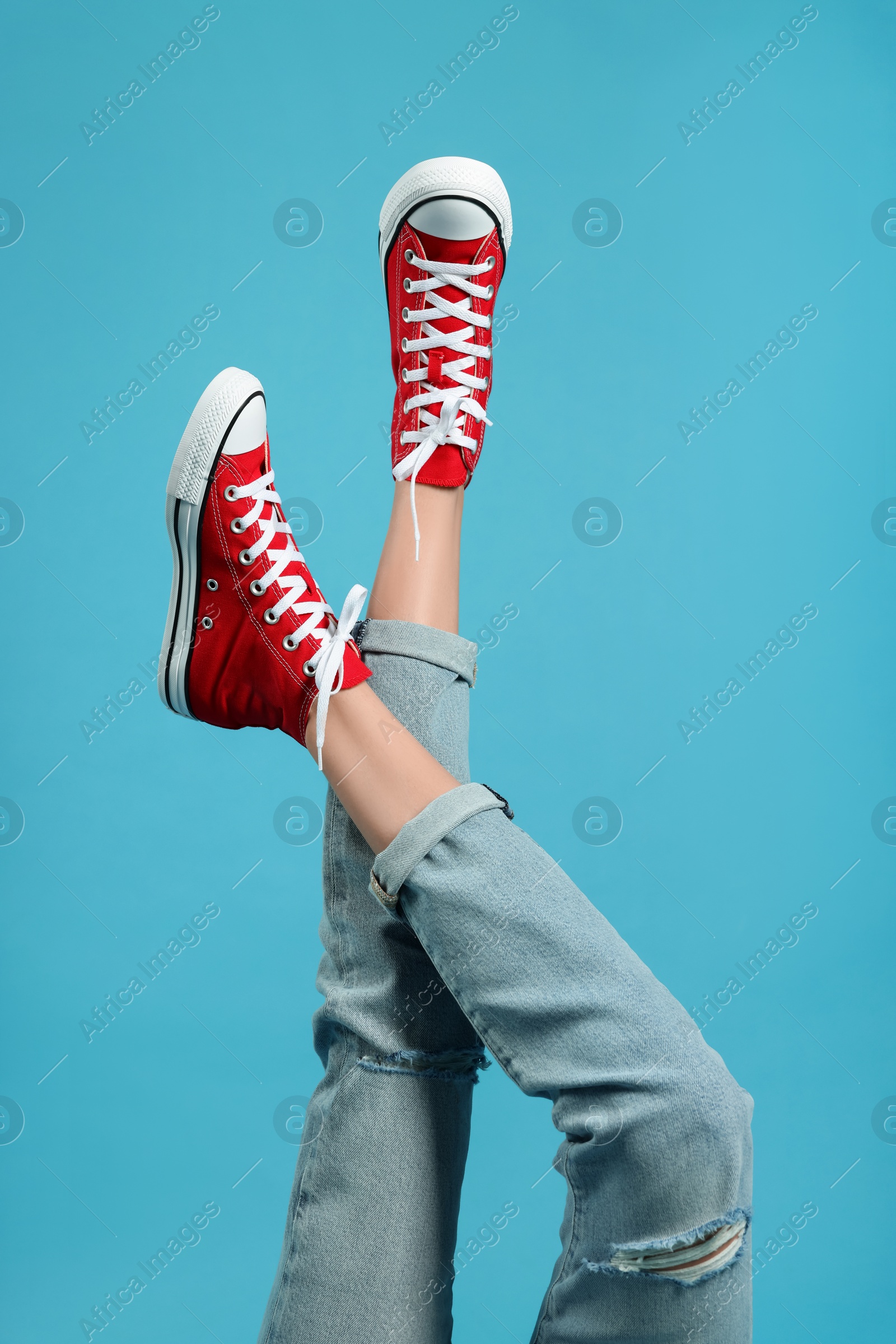 Photo of Woman in stylish gumshoes on light blue background, closeup