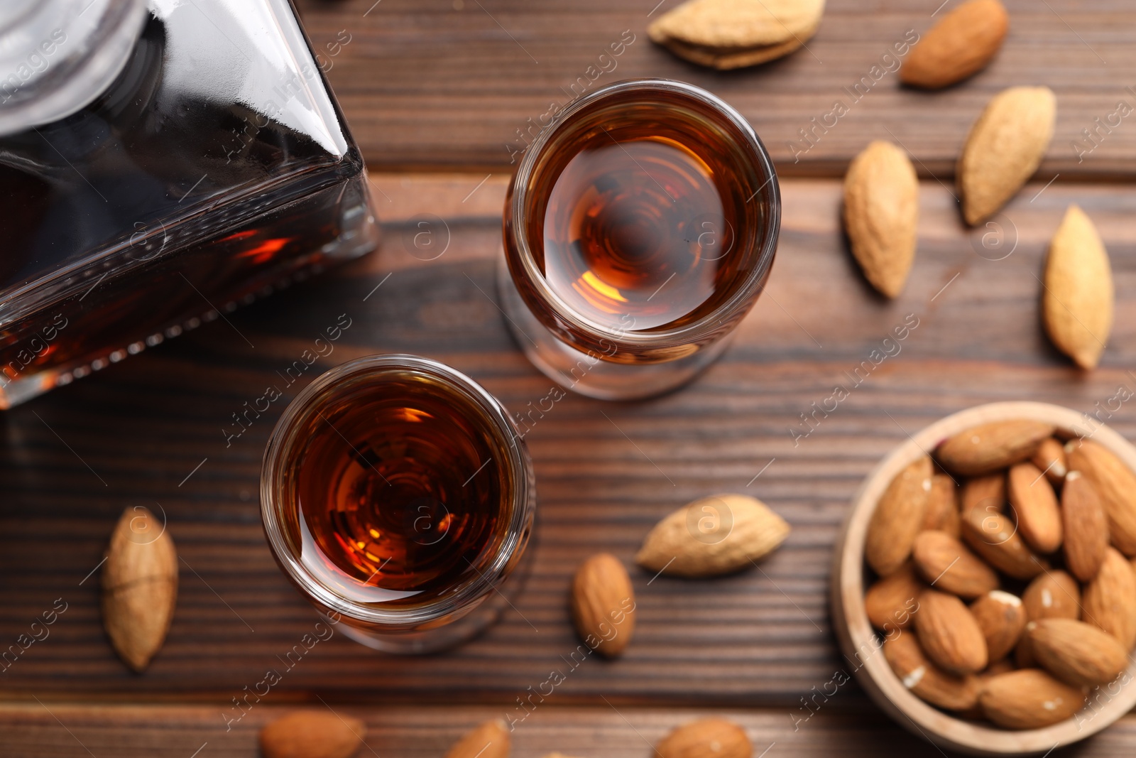 Photo of Liqueur glasses with tasty amaretto and almonds on wooden table, flat lay