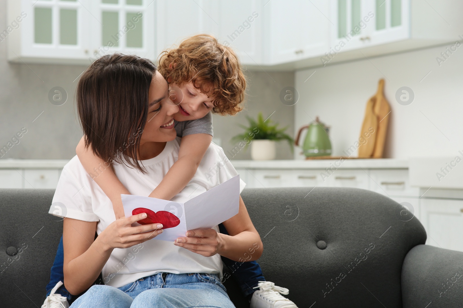 Photo of Little son congratulating his mom with Mother`s day at home. Woman holding greeting card