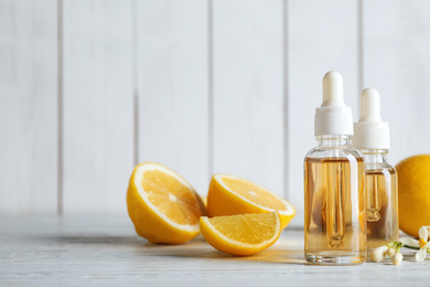 Photo of Bottles of citrus essential oil and lemons on white wooden table. Space for text