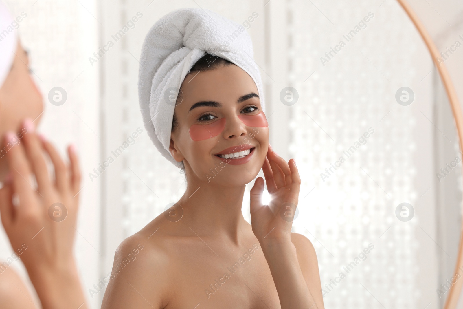 Photo of Beautiful young woman with under eye patches near mirror at home