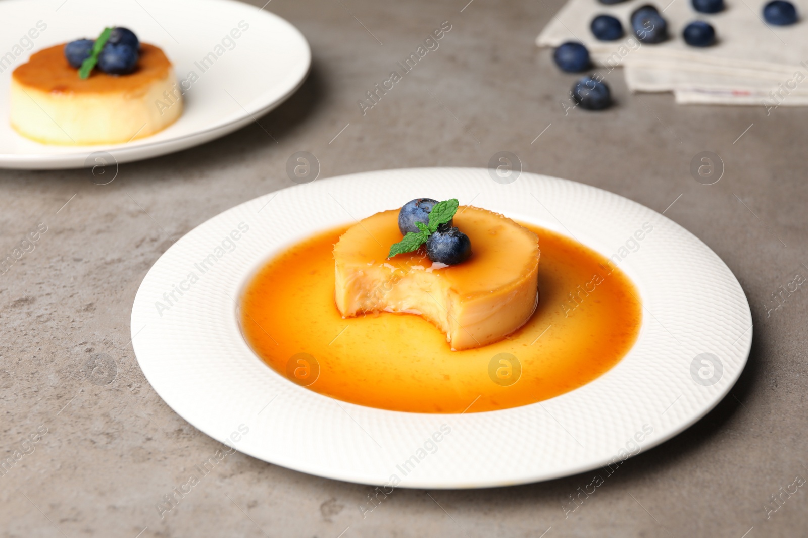 Photo of Delicious puddings with caramel and blueberries on grey table