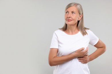 Beautiful senior woman doing breast self-examination on light grey background, space for text