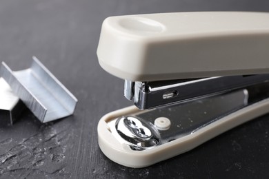Photo of Beige stapler with staples on black textured table, closeup