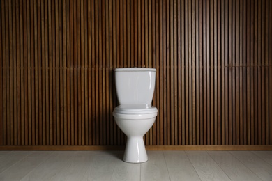 Photo of New toilet bowl near wooden wall indoors