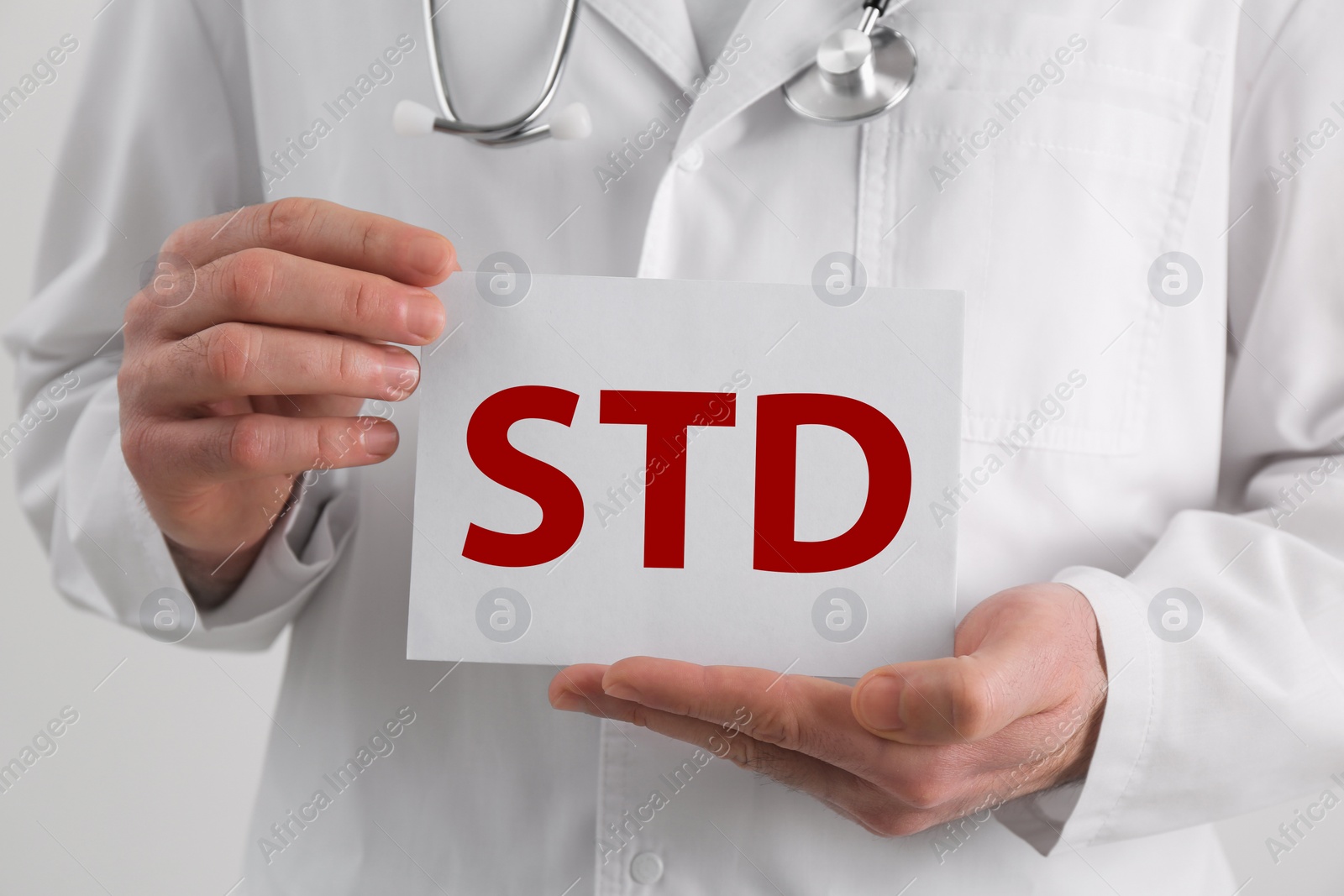 Photo of Doctor holding sheet of paper with abbreviation STD on white background, closeup