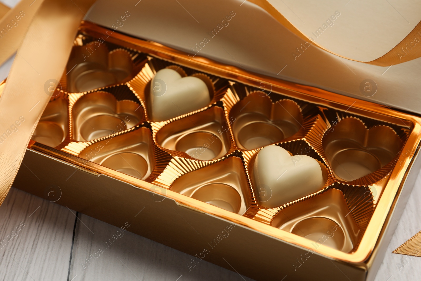 Photo of Partially empty box of chocolate candies on white wooden table, closeup