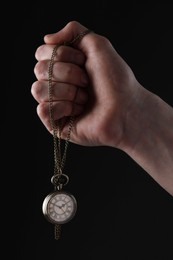 Man holding chain with elegant pocket watch on black background, closeup