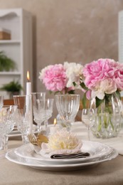 Stylish table setting with beautiful peonies and burning candles indoors