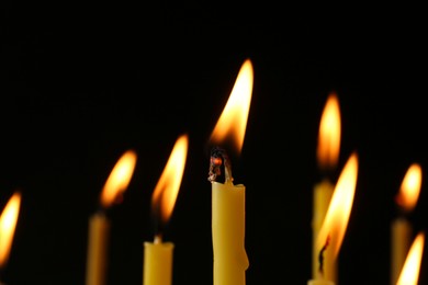 Photo of Burning church candles on black background, closeup