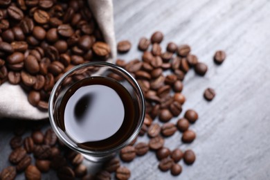 Photo of Glass of coffee liqueur and beans on grey table, top view. Space for text
