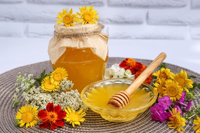 Photo of Delicious honey and different flowers on wicker mat against white brick wall