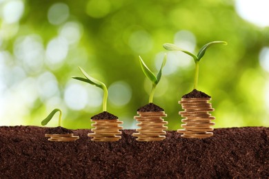 Stacked coins and green seedlings on ground outdoors, bokeh effect. Investment concept