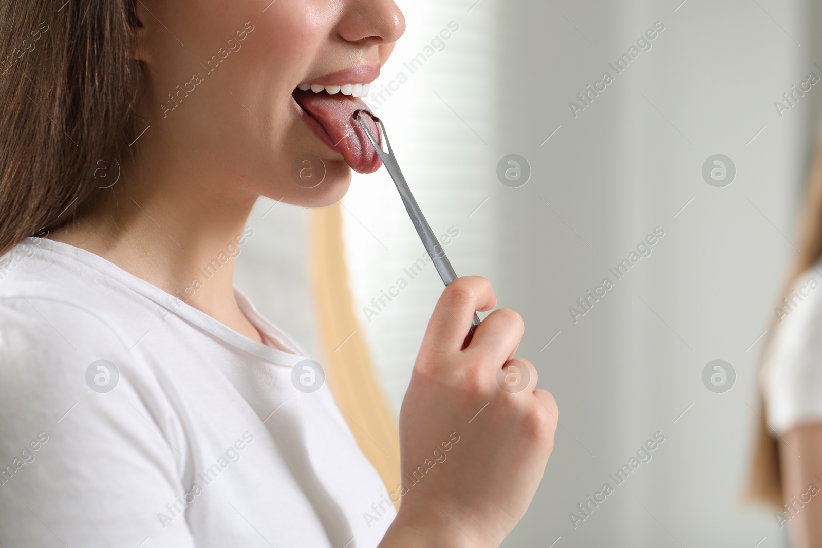 Photo of Woman brushing her tongue with cleaner on blurred background, closeup. Space for text