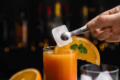 Bartender putting ice cube into glass with Tequila Sunrise cocktail, closeup
