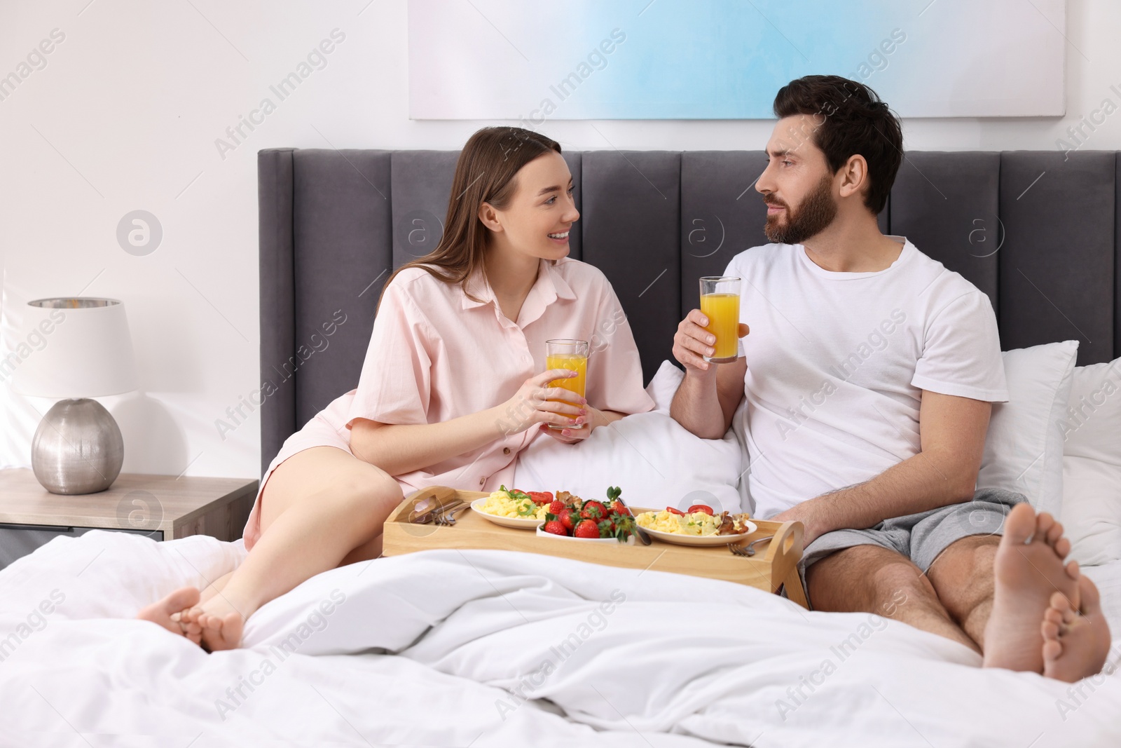 Photo of Happy couple having breakfast and talking on bed at home