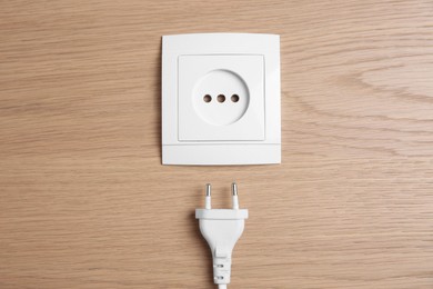 Photo of Power socket with plug on wooden table, flat lay