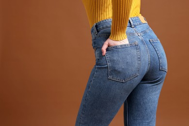Photo of Woman in stylish jeans on brown background, closeup. Space for text
