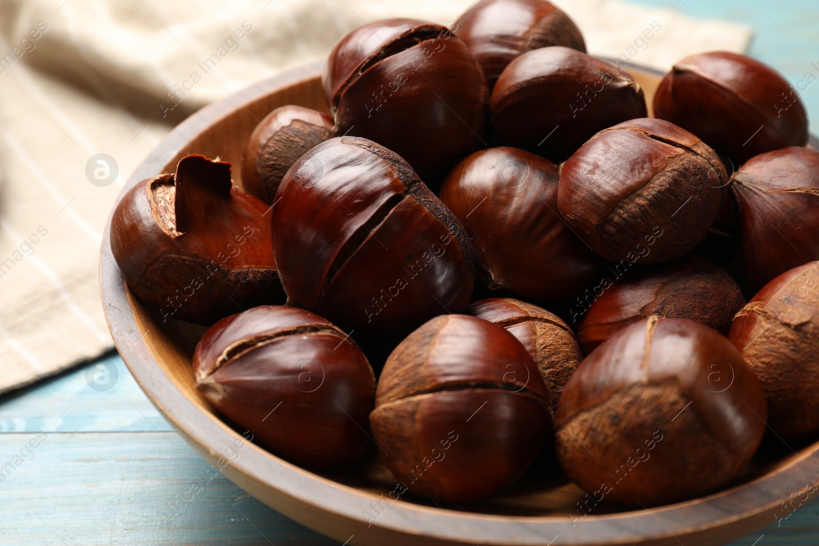 Photo of Fresh edible sweet chestnuts in bowl on light blue wooden table, closeup