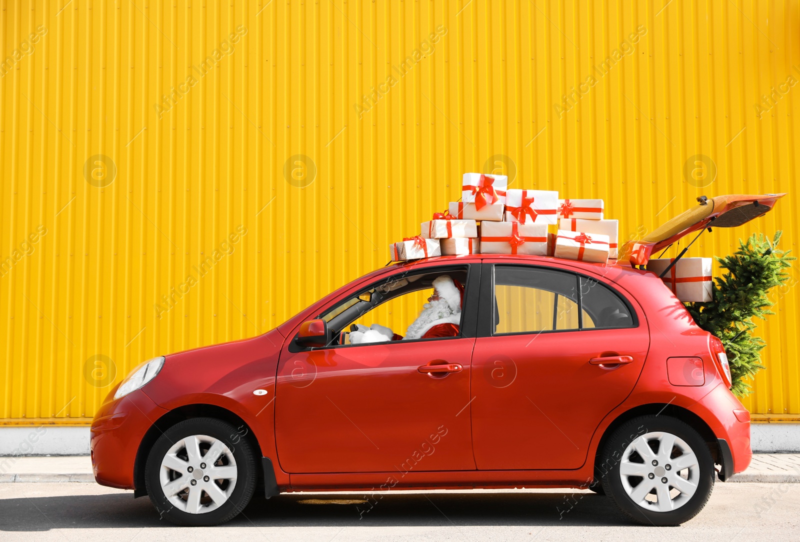 Photo of Authentic Santa Claus driving red car with gift boxes and Christmas tree, view from outside