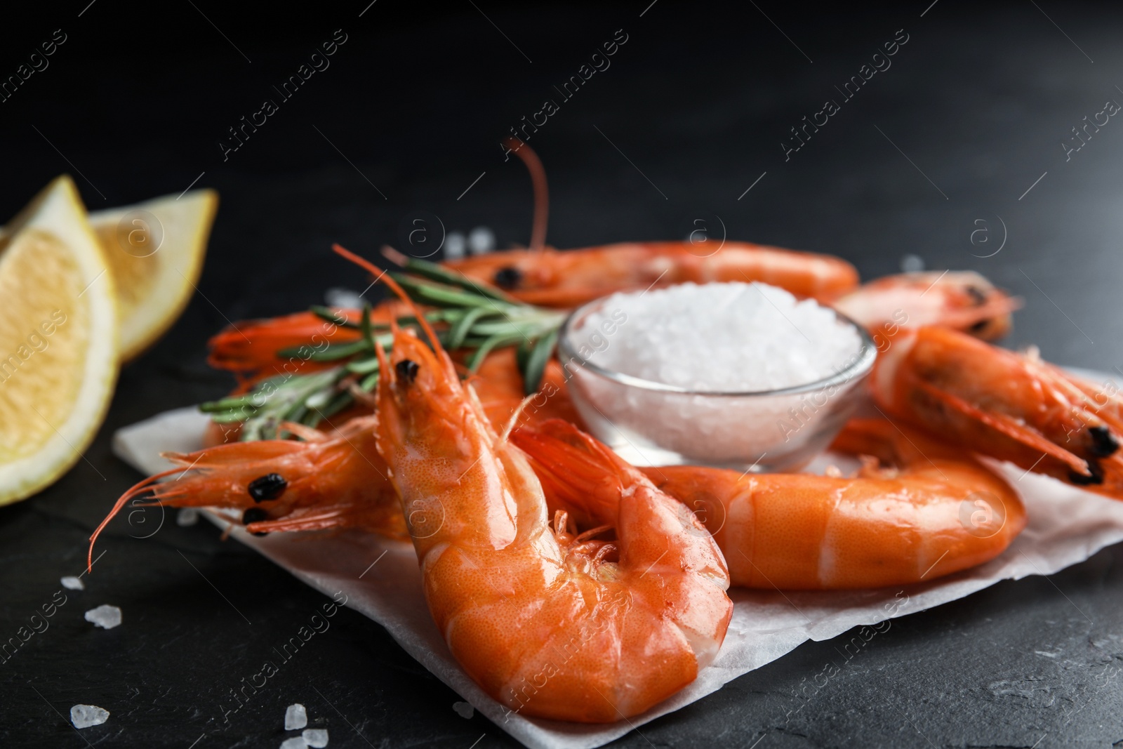 Photo of Delicious cooked shrimps and salt on black table