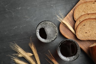 Photo of Delicious kvass, bread and spikes on black slate table, flat lay