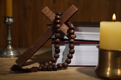 Photo of Bible, cross, rosary beads and church candles on wooden table