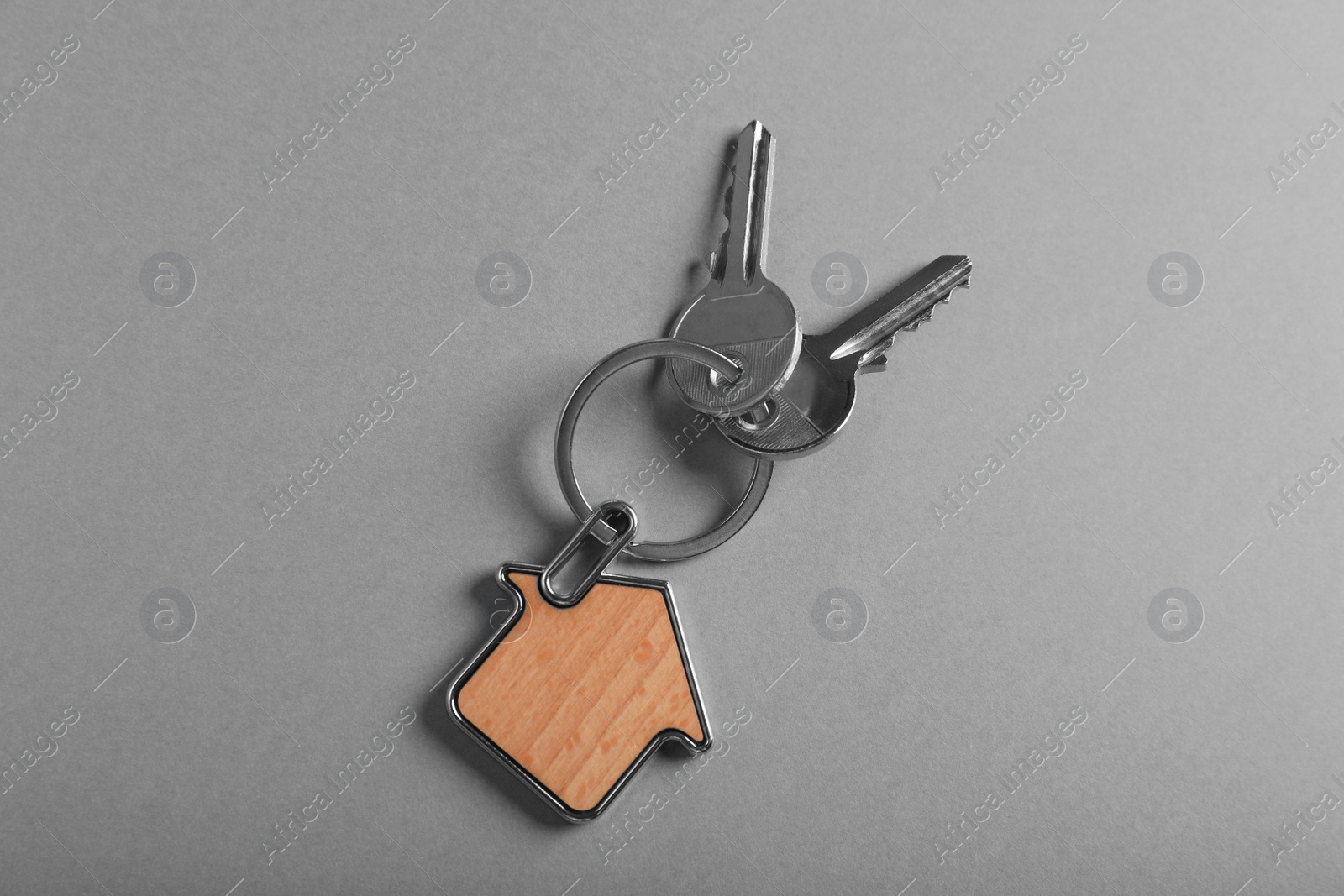 Photo of Keys with trinket in shape of house on grey background, top view. Real estate agent services