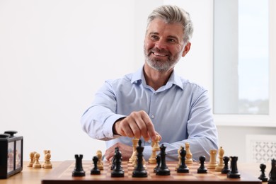 Photo of Happy man playing chess during tournament at table indoors