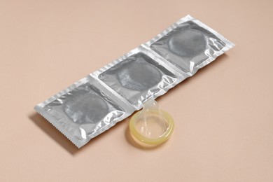 Photo of Unpacked condom and packages on beige background. Safe sex