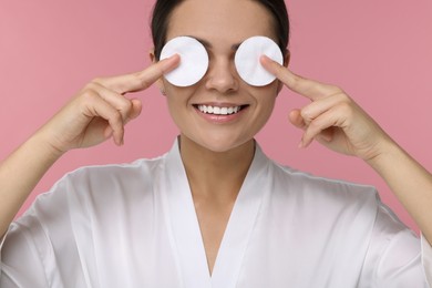 Photo of Young woman covering her eyes with cotton pads on pink background