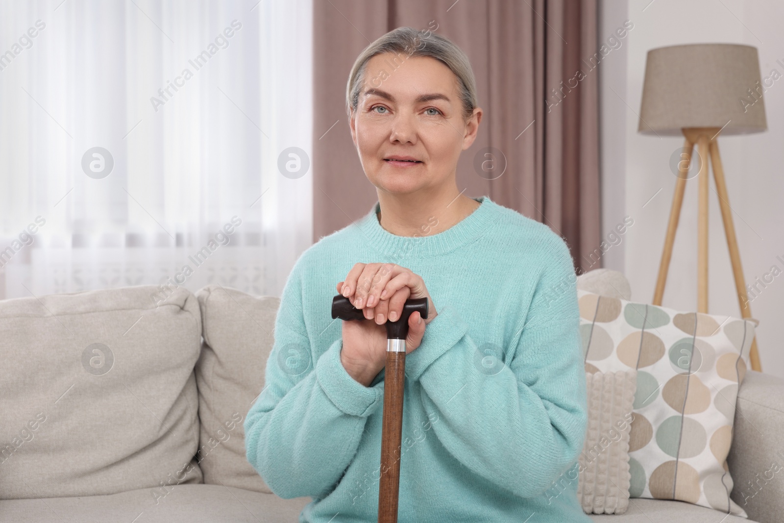 Photo of Senior woman with walking cane sitting on sofa at home