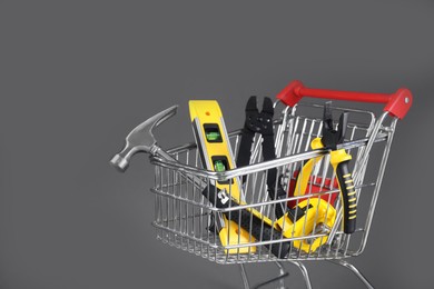 Photo of Small shopping cart with set of construction tools on grey background