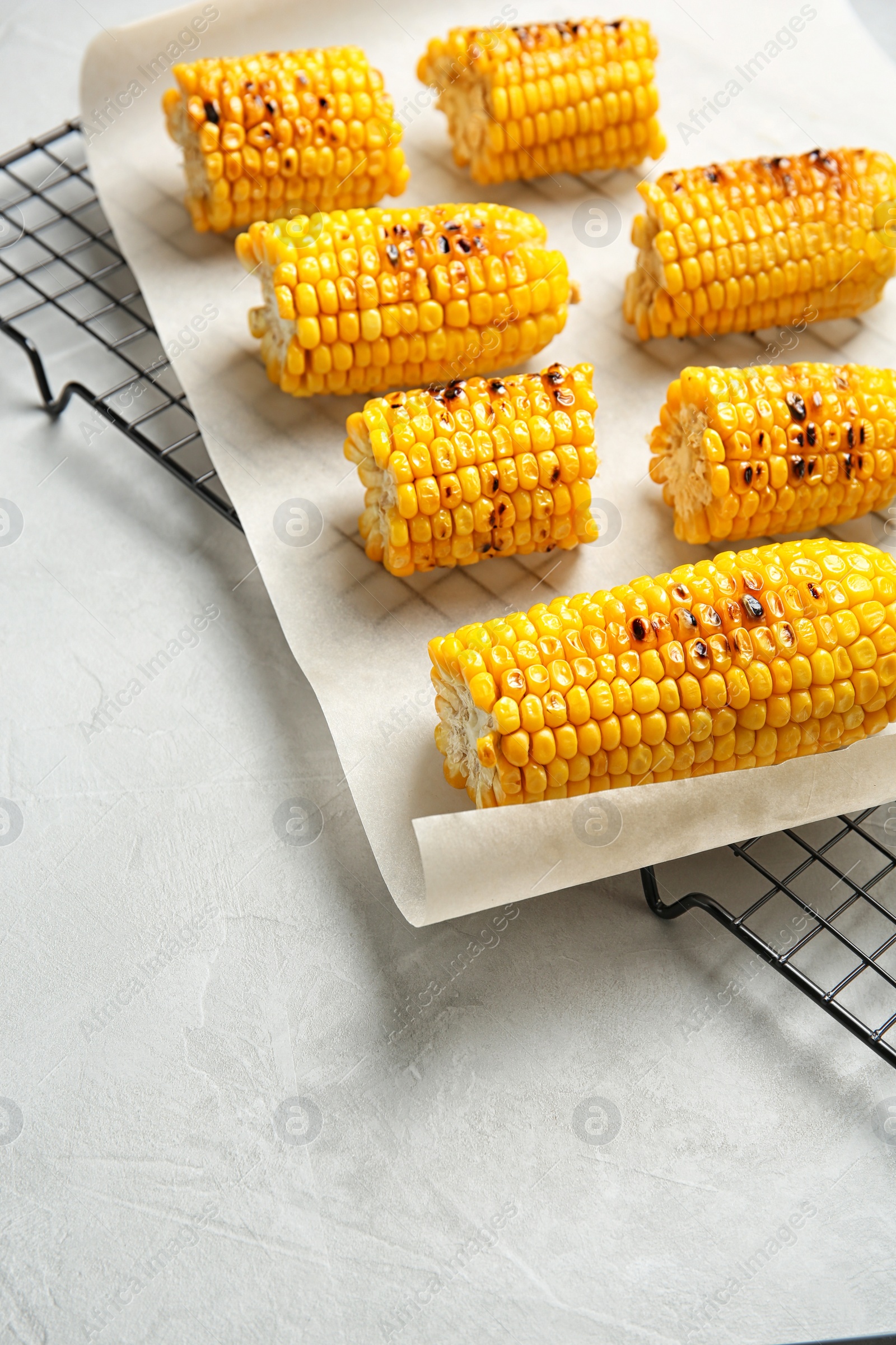 Photo of Cooling rack with grilled corn cobs on light background