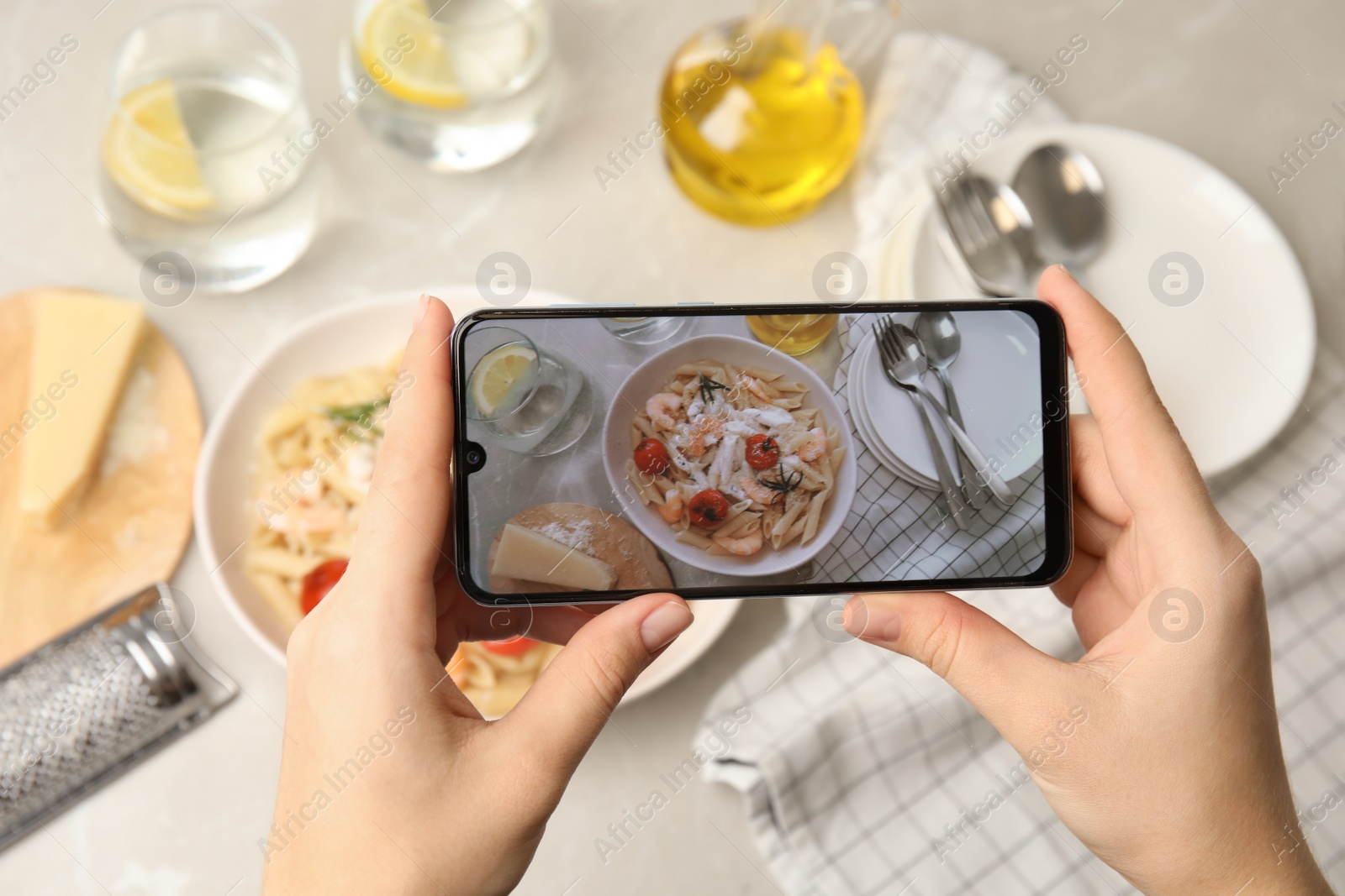 Photo of Food blogger taking picture of tasty pasta with shrimps and tomatoes at light table, closeup