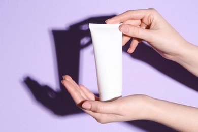 Photo of Woman holding tube of cream on violet background, closeup