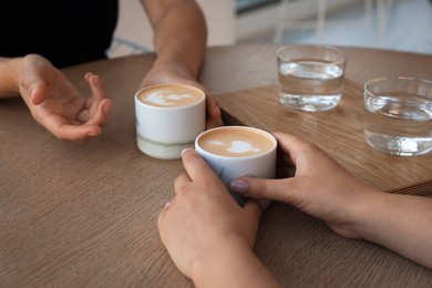 Friends drinking coffee at wooden table in cafe, closeup