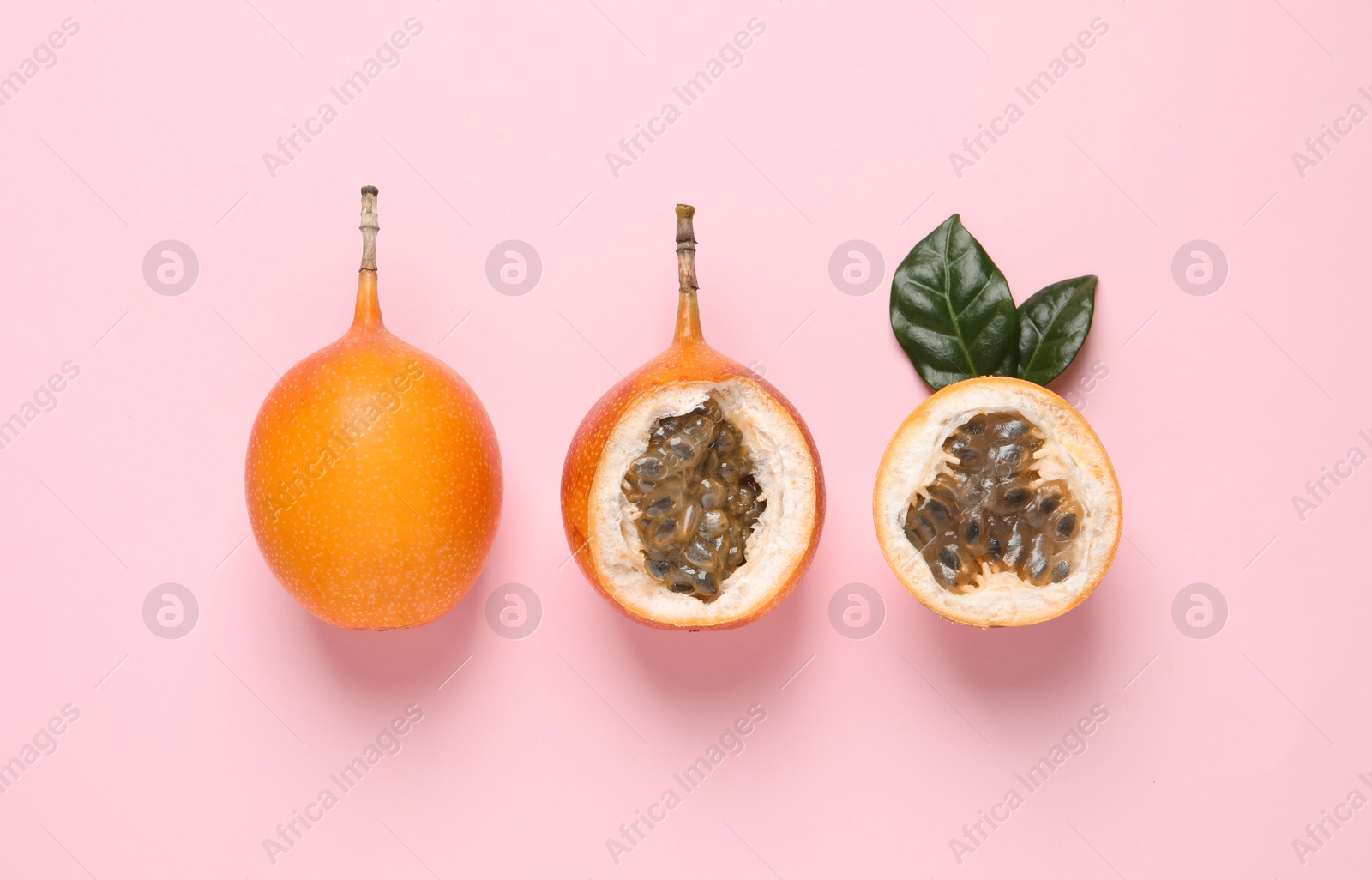 Photo of Delicious ripe granadillas with leaves on pink background, flat lay