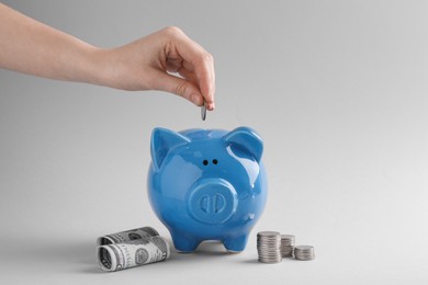 Photo of Financial savings. Woman putting coin into piggy bank on grey background, closeup