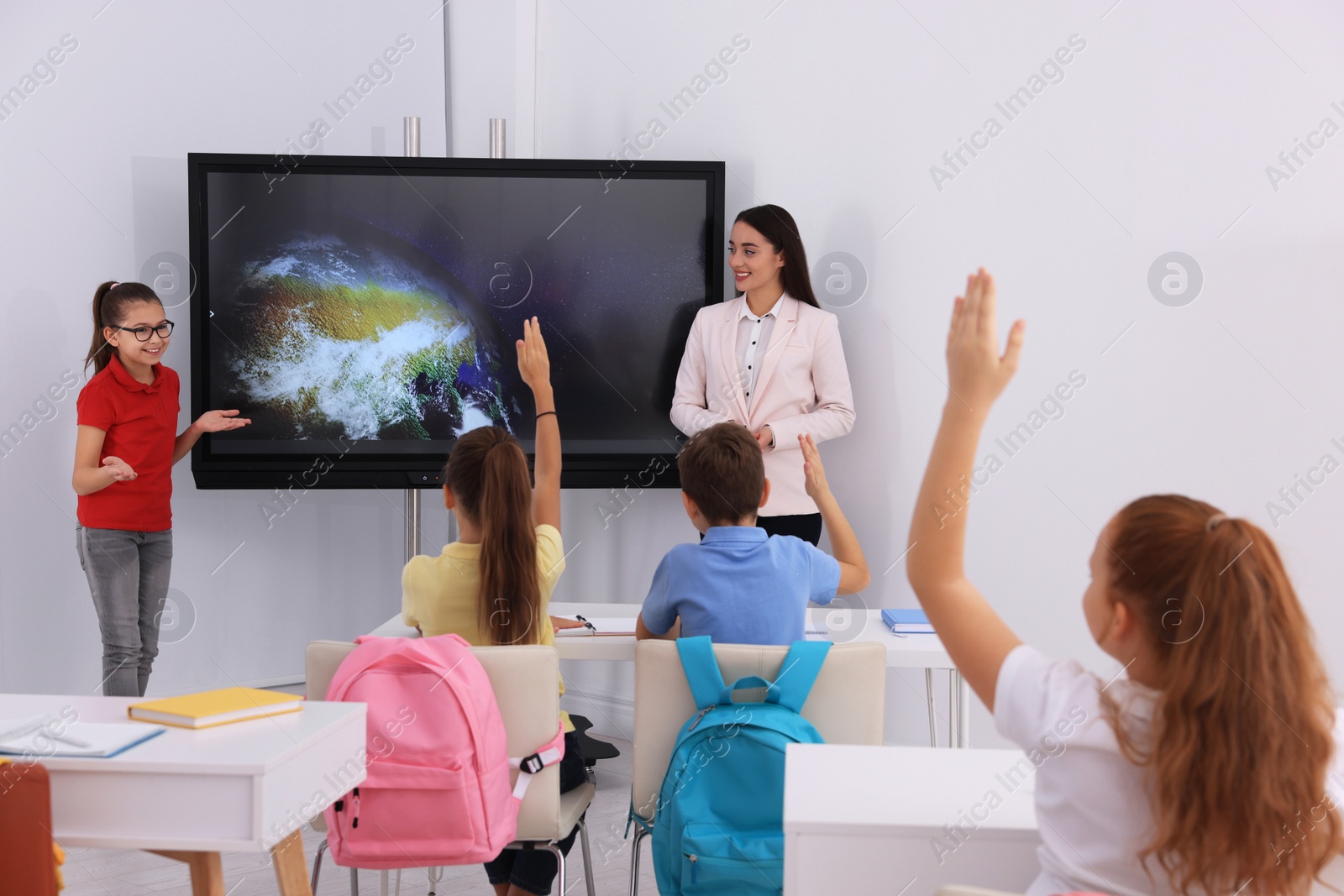 Photo of Teacher and pupil near interactive board in classroom during lesson