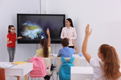 Photo of Teacher and pupil near interactive board in classroom during lesson