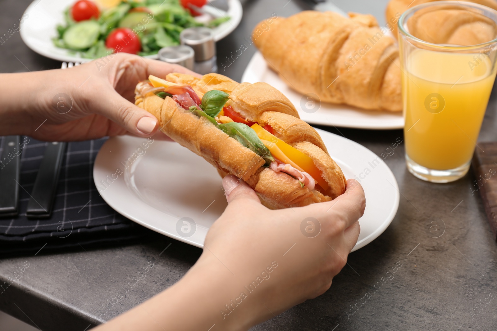 Photo of Woman holding tasty croissant sandwich over plate at table